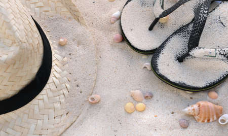 straw hat and flip flops on the sand with seashellsの写真素材