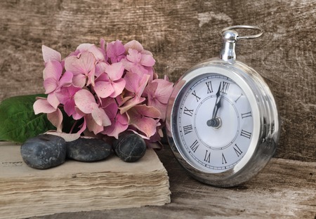 retro clock at twelve soon  with flowers on old book on wooden background