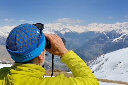 hiker looking the snowy mountain with binocularsの写真素材
