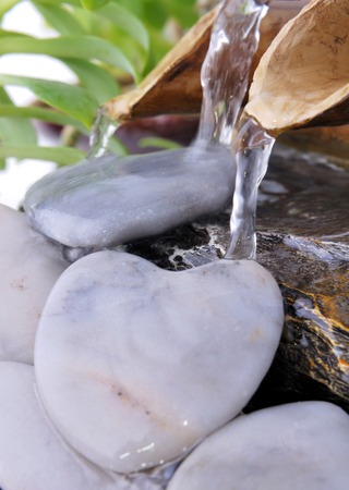 water flowing from little bamboo fountain on heart-shaped pebblesの写真素材
