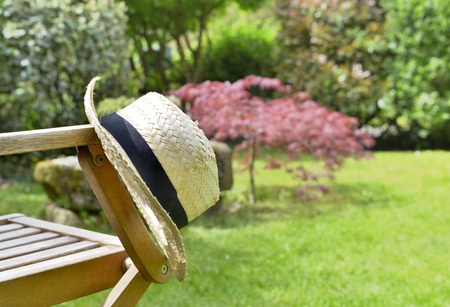 close on straw hat put on a wooden chair in an ornamental gardenの写真素材