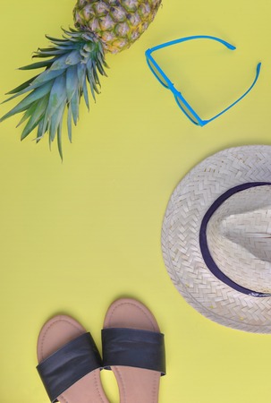 top view on female sandale straw hat, sunglasses and pineapple on yellow backgroundの写真素材