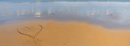 heart drawing on the sand in front of the seaの写真素材