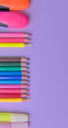 group of colorful pencils and pens arranged in line on the left and a copy space on the right on mauve backgroundの写真素材