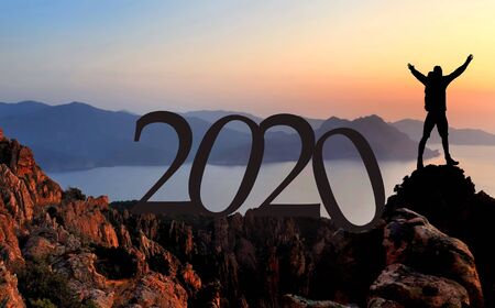 2020 number and a silhouette of hiker enjoying at the top of cliff overlooking the sea at sunset