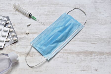 surgical blue  mask on a table with pills, hand sanitizer and syringue on white table