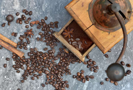 top view on old coffee grinder full of coffee and beans with spices on gray marble bacground