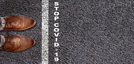 top view on foot behind a line drawing on asphalt with text stop covid-19