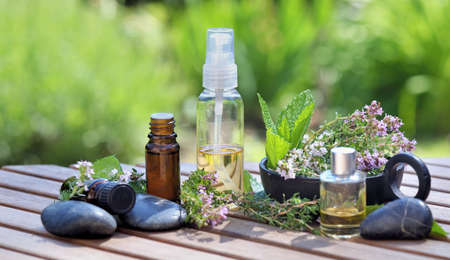 bottles of essential oils on a table with aromatic herbs abd black tones flowersの写真素材