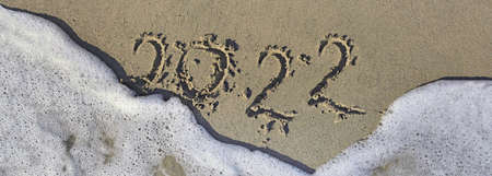 2022 written in the sand of a beach on the edge of the foam of wave in panoramic viewの写真素材