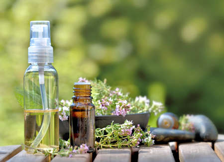 bottles of essential oil and flowers of aromatic herb on a table and on green backgroundの写真素材