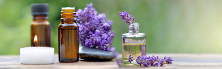 bottles of essential oil among lavender flowers arranged on a wooden table with canddle and pebbleの写真素材
