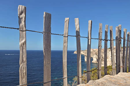 wooden coastline fence on stoned wall in front of blue sea and sky at Bonifacio in Corsicaの写真素材
