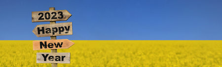 2023 happy new year written on a direction sign in front of field of yellow rapeseed rapeseed blooming under blue sky colors of ukrainian flagの写真素材