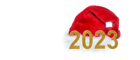 year 2023 golden numbers in front of red santa claus hat on white backgroundの写真素材