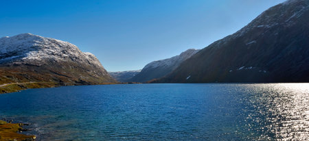 beautiful view of a blue water in a fjord in norway with snow-capped mountains under blue skyの写真素材