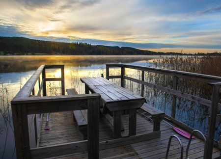 wooden dock with a table at the edge of a lake at dusk in beautiful Sweden landscapeの写真素材