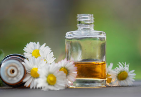 bottles of essential oil and daisies with fresh mint leaf on a wooden table outdoorsの写真素材