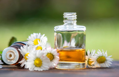 bottles of essential oil and daisies with fresh mint leaf on a wooden table outdoorsの写真素材