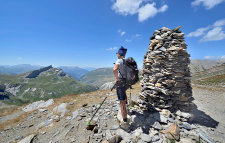 a hiker standing next to a big cairn on the trail of the tour of Mont Blanc in summer and looking at mountainsの写真素材