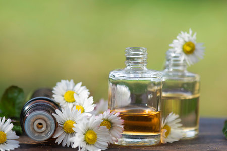 bottles of essential oil and daisies with fresh mint leaf on a wooden table outdoorsの写真素材