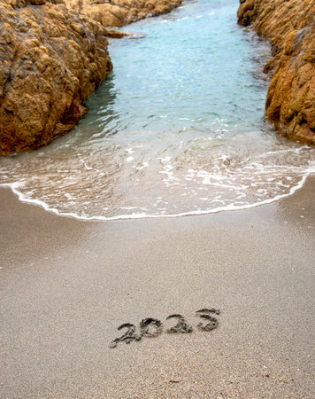 2025 handwritten on the sand of a beach with a wave passing between rocksの写真素材