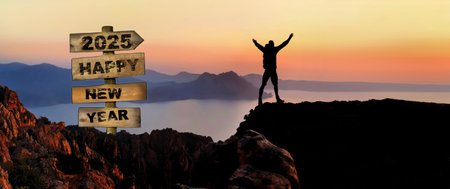 2025 happy new year written on wooden post sign and silhouette of hiker with their arms up on a cliiff in seascape in front of sunsetの写真素材