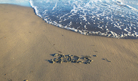 2025 text handwriting on the sand in a beach with a wave at ocean beach shoreの写真素材