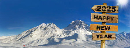 2025 happy new year written on wooden sign and panoramic view on snowy peak mountain under sunny blue skyの写真素材