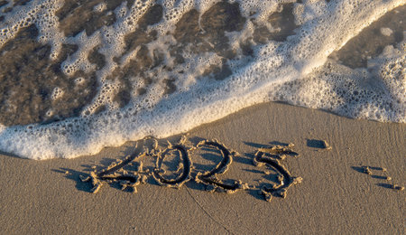 2025 text handwriting on the sand in a beach with a wave at ocean beach shoreの写真素材