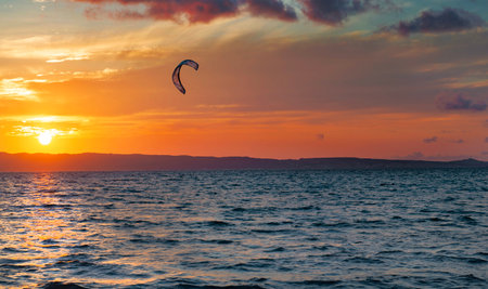 sunset over the sea with a kite surf sail under a colorful skyの写真素材