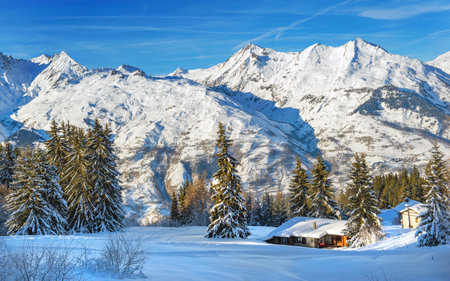 winter landscape in mountain covered with snow under blue sky and chalet at the foot of mountains in a ski resort in tarentaise - franceの写真素材