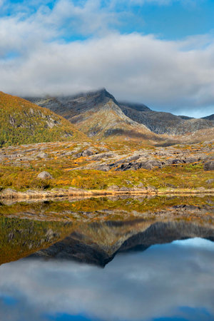 mountain and autumnal forest under the sky reflecting in surface of water in Norway.の写真素材