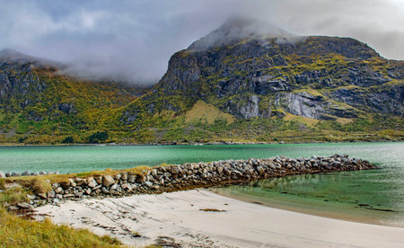 beautiful emerald water of a Norwegian fjord at the foot of the mountains with a stone jetty on the island of Flakstadoya in the archipelago of Lofotenの写真素材