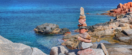 red and gray pebbles stacked on the rock in front of beautiful sea of Sardinia islandの写真素材