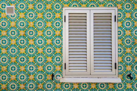 typical geometric colorful tile Azulejos mosaic on facade with window closed of a house in Portugal