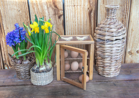 chicken eggs in a decorative box put on a table next to flower potted and a vase on wooden backgroundの写真素材