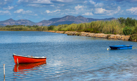 pretty red boat moored in the sea with mountain in background under blue skyの写真素材