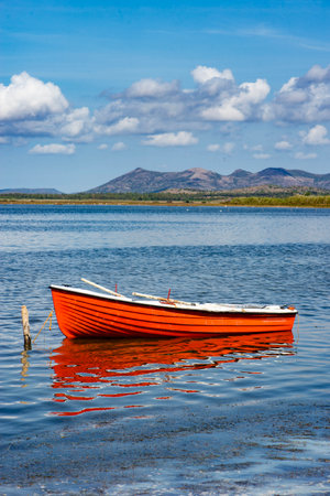 pretty red boat moored in the sea in Sardinia with mountain in background under blue skyの写真素材