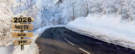 2026 HAPPY NEW YEAR written on wooden POST sign with arrow pointing to a road crossing a snowy...