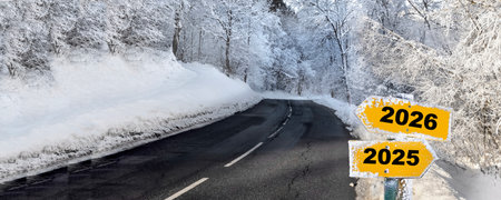 2026 and 2025 written on yellow post sign with two arrows pointing opposite on a road crossing a snowy forest in alpine mountainの写真素材