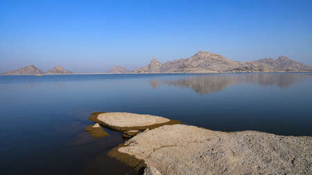 A selective focus image of a  landscape of Jawai dam with clear blue sky and Aravalli mountain ranges with its reflection in water at Jawai in Rajasthan  Indiaの写真素材
