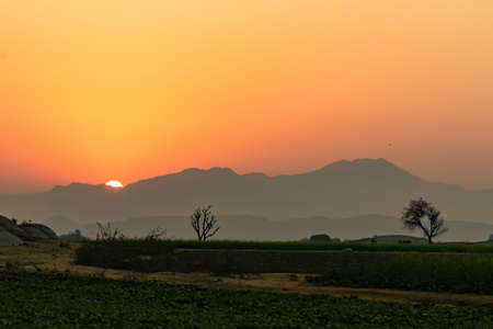 An image with dynamic range of Sun rise from behind the Aravalli mountain ranges seen as silhouette  from Jawai bandh in Rajasthan Indiaの写真素材