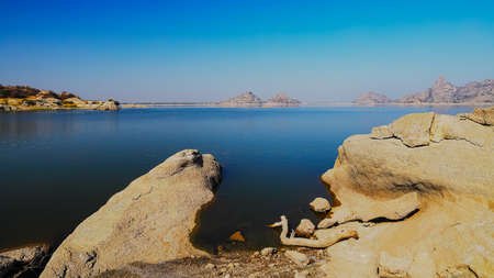 A selective focus image of a  landscape of Jawai dam with clear blue sky and Aravalli mountain ranges with its reflection in water at Jawai in Rajasthan  Indiaの写真素材