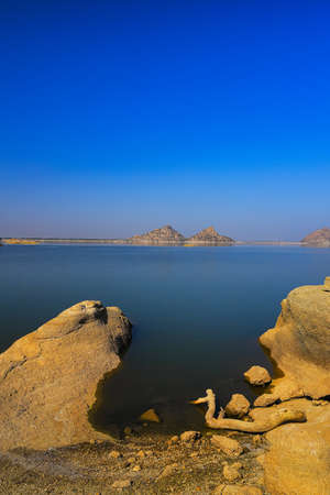 A selective focus image of a  landscape of Jawai dam with clear blue sky and Aravalli mountain ranges with its reflection in water at Jawai in Rajasthan  Indiaの写真素材