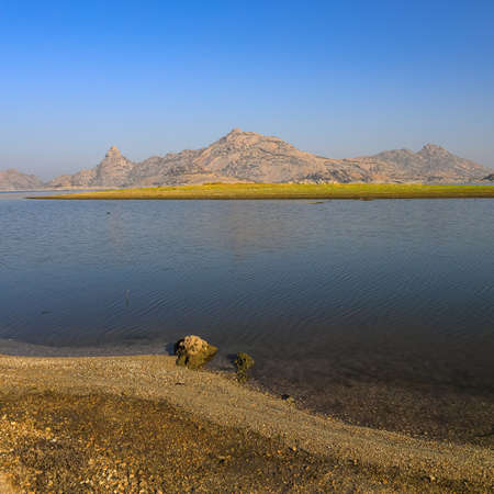 A selective focus image of a  landscape of Jawai dam with clear blue sky and Aravalli mountain ranges with its reflection in water at Jawai in Rajasthan  Indiaの写真素材