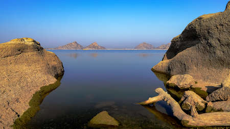 A selective focus image of a  landscape of Jawai dam with clear blue sky and Aravalli mountain ranges with its reflection in water at Jawai in Rajasthan  Indiaの写真素材