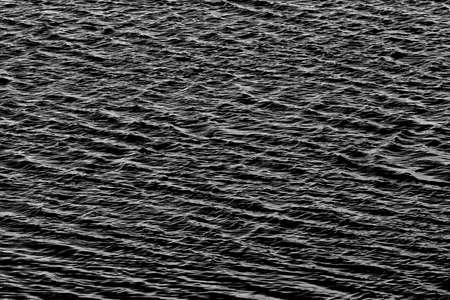 A grainy abstract image in monochrome of ripples on water creating a pattern which can be used for background or tiles or writing a messageの写真素材