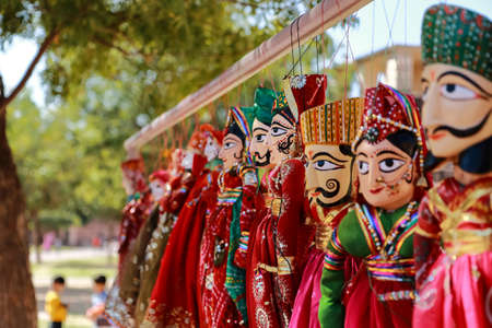 Colorful human face shaped Puppets wearing colorful clothes hanging against the wall in Rajasthan...