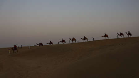 A line of camels walking on Sam sand dunes with people siting on themの写真素材